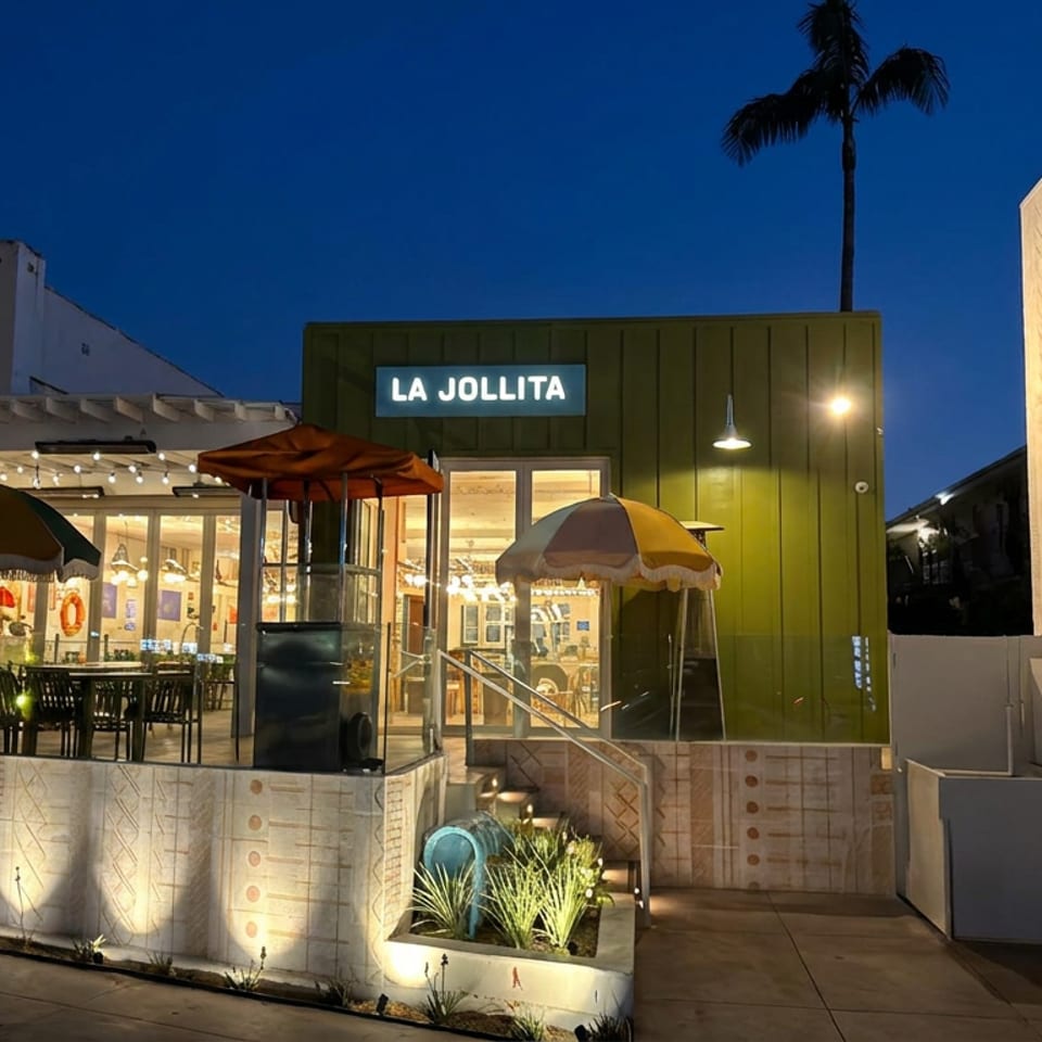La Jollita restaurant exterior illuminated at dusk, featuring a green entrance, outdoor patio seating, umbrellas, and string lights.